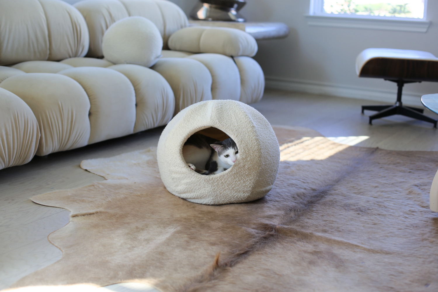 luxury cat bed by catenary home that is a cat cave with a grey and white cat in a modern living room on the floor of a cowhide rug