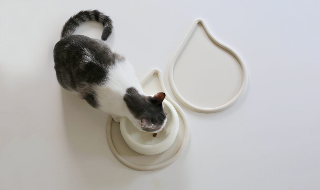 raindrop shape cat food mat by catenary home can also be used as dog food mat with grey and white cat eating from bowl