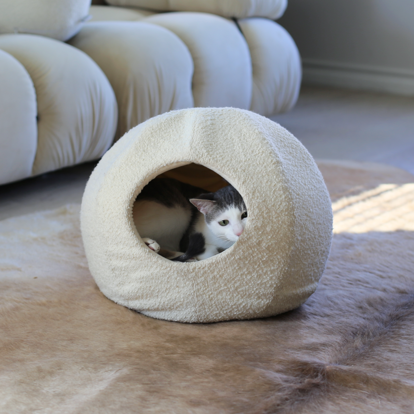 modern cat bed cave in white boucle on living room floor with grey and white cat inside by catenary home is like a cat igloo, cat nest and cat hideaway all in one
